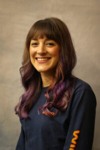A woman with purple hair smiles for the camera.